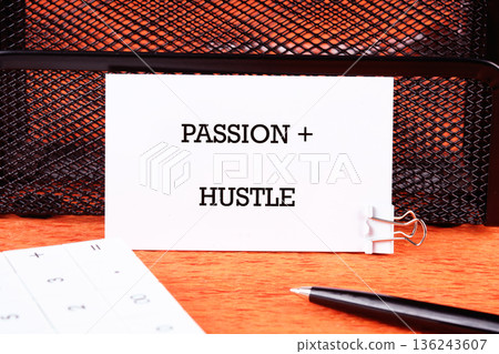 White card displaying the inspiring message Passion plus Hustle. It stands on a wooden desk with a calculator and a black pen for work 136243607
