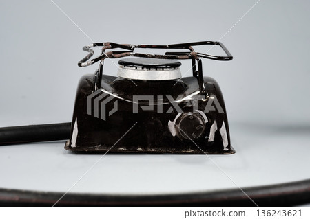 A sturdy black portable gas stove sits ready for use, displaying its single burner and control knob. A fuel hose extends from its side A sturdy black portable gas stove sits ready for use, displaying its single burner and control knob. A fuel hose extends from its side 136243621