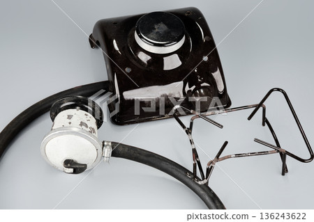 A dark portable gas stove burner, a silver gas regulator with a black hose, and a metal pot support rest on a grey background A dark portable gas stove burner, a silver gas regulator with a black hose, and a metal pot support rest on a grey background 136243622