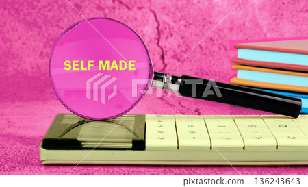 A pink magnifying glass shows the words self made over a calculator. Nearby are stacked blue, orange, and red books A pink magnifying glass shows the words self made over a calculator. Nearby are stacked blue, orange, and red books 136243643