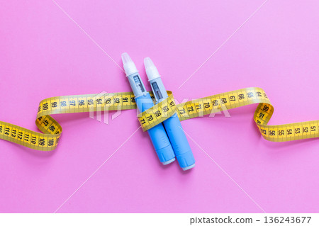 Blue insulin pens and yellow measuring tape on pink background representing weight loss, diabetes treatment, healthcare, and medical control. drugs injection ozempic for weight loss 136243677