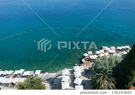 Aerial view of Opatija beach in Croatia with turquoise Adriatic Sea, white parasols, sunbeds, and swimmers enjoying a sunny summer. Scenic seaside resort in Opatija, Croatia, clear blue water. 136243693