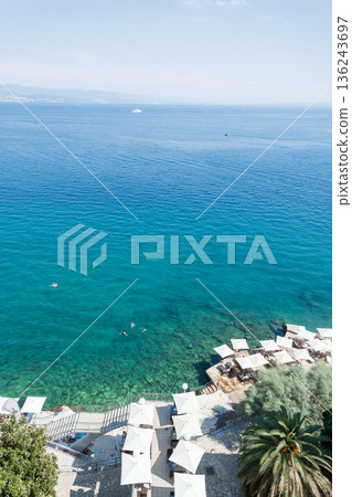 Aerial view of Opatija, Croatia, with turquoise Adriatic Sea, swimmers, beach umbrellas, and a scenic coastline. Popular summer travel destination on the Croatian Riviera 136243697