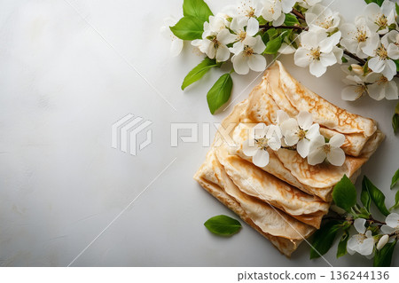 Golden crepes garnished with white spring blossoms, symbolizing seasonal renewal and cultural festivities like shrove tuesday and maslenitsa copy space 136244136