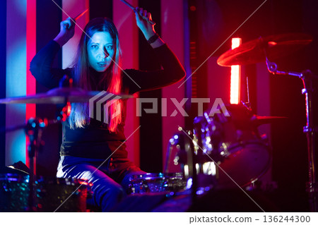 Energetic female drummer performing live music under vibrant stage lights 136244300