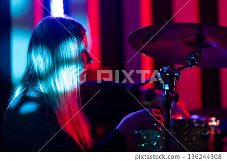 Female drummer performing music under vibrant stage lights 136244308