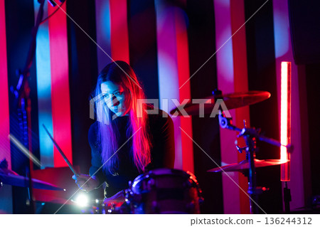 Young woman drummer playing music with vibrant neon lights Young woman drummer playing music with vibrant neon lights 136244312