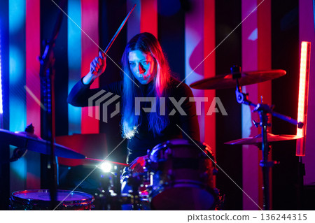 Woman drummer playing drums under neon lights Woman drummer playing drums under neon lights 136244315