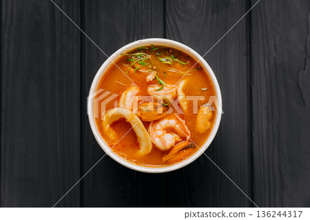 Tom yum soup with shrimp, mussels and squid in kraft bowl on dark wooden table Tom yum soup with shrimp, mussels and squid in kraft bowl on dark wooden table 136244317