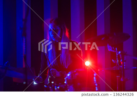 Female musician playing drums illuminated by neon stage lights Female musician playing drums illuminated by neon stage lights 136244326