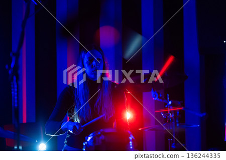 Female drummer performing on stage with blue red lighting 136244335