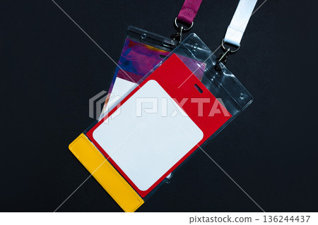 Blank identification badge in a plastic holder with red, white, and yellow colors, hanging on a lanyard. Concept of access, event pass, or personal credentials. Free copy space for design 136244437