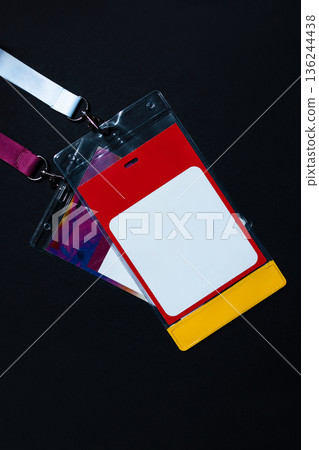 Blank ID badge with red, white, and yellow design on a white lanyard, isolated on black background. Ideal for events, conferences, staff identification, or access control concepts 136244438