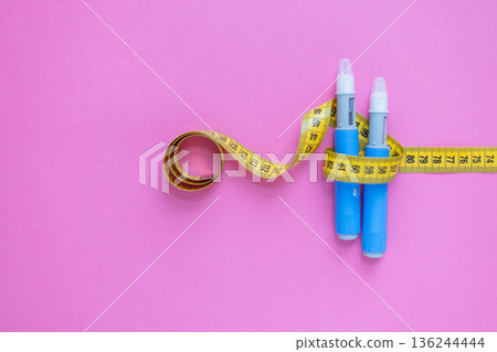 Concept image of diabetes and obesity treatment with two insulin pens and a measuring tape on pastel background. drugs injection ozempic for weight loss 136244444