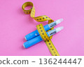Weight loss and insulin therapy concept. Blue injection pens and yellow measuring tape arranged creatively on pink background. drugs injection ozempic for weight loss 136244447