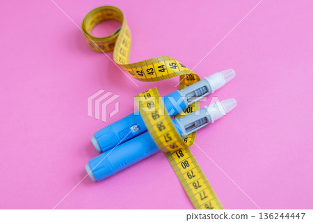 Weight loss and insulin therapy concept. Blue injection pens and yellow measuring tape arranged creatively on pink background. drugs injection ozempic for weight loss Weight loss and insulin therapy concept. Blue injection pens and yellow measuring tape arranged creatively on pink background. drugs injection ozempic for weight loss 136244447