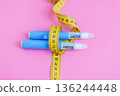 Close-up of insulin pens tied with measuring tape on pink background, symbolizing control of diabetes and healthy body weight. drugs injection ozempic for weight loss 136244448