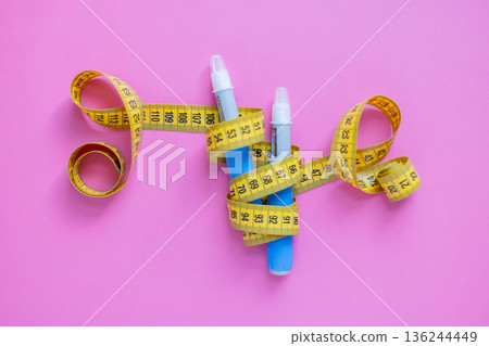 Insulin injection pens and measuring tape on pink surface. Concept of obesity control, diabetes care, and modern medication. drugs injection ozempic for weight loss Insulin injection pens and measuring tape on pink surface. Concept of obesity control, diabetes care, and modern medication. drugs injection ozempic for weight loss 136244449