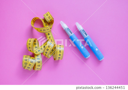 Two blue insulin pens and a yellow measuring tape on a pink background, symbolizing weight loss, diabetes treatment, and medical control. drugs injection ozempic for weight loss Two blue insulin pens and a yellow measuring tape on a pink background, symbolizing weight loss, diabetes treatment, and medical control. drugs injection ozempic for weight loss 136244451