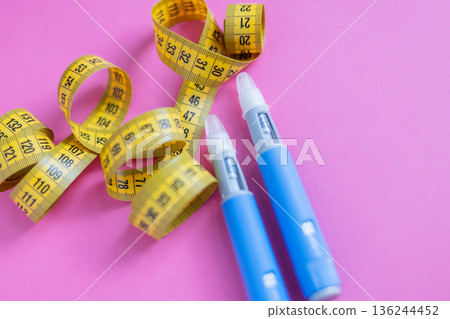 Blue insulin pens next to curled yellow measuring tape. Healthcare, weight management, and diabetes support theme. drugs injection ozempic for weight loss Blue insulin pens next to curled yellow measuring tape. Healthcare, weight management, and diabetes support theme. drugs injection ozempic for weight loss 136244452
