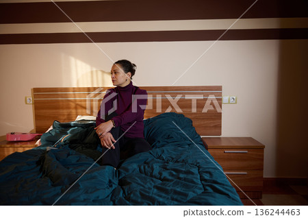 Woman Seated On Bed In Cozy Bedroom With Purple Sweater And Blue Comforter Woman Seated On Bed In Cozy Bedroom With Purple Sweater And Blue Comforter 136244463