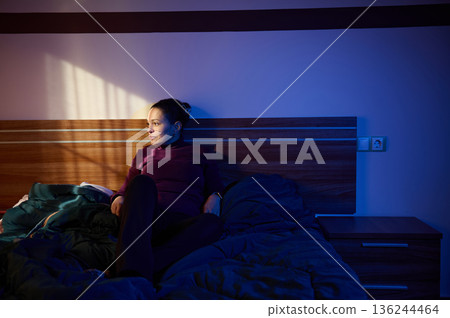 Woman Relaxing On Bed In Dim Blue Night Lighting With Sunlit Shadow Across Bedroom Woman Relaxing On Bed In Dim Blue Night Lighting With Sunlit Shadow Across Bedroom 136244464