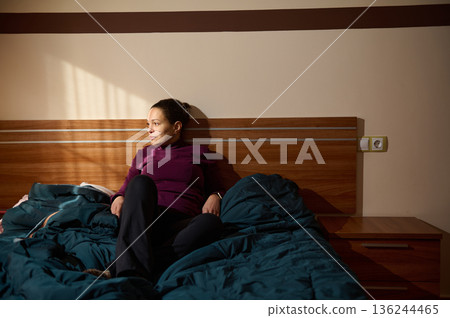 Woman Relaxing On Bed In A Cozy Bedroom With Purple Top And Blue Duvet, Morning Light 136244465