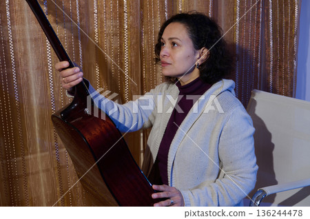 Woman With Acoustic Guitar In A Cozy Home Setting Adjusting The Instrument 136244478