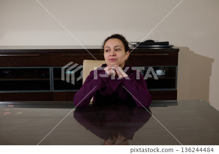 Thoughtful Woman Seated at Glass Table in a Modern Office Setting Thoughtful Woman Seated at Glass Table in a Modern Office Setting 136244484