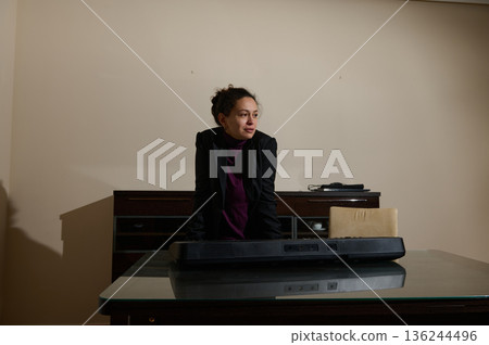 Professional Woman in Office Leaning Over Desk with Keyboard in Modern Studio Setting 136244496