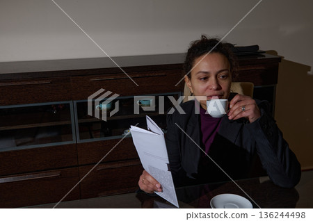 Business Woman Sips Coffee While Reading Document At Office Desk Business Woman Sips Coffee While Reading Document At Office Desk 136244498