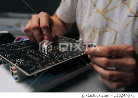 Technician hands removing old thermal paste from CPU of computer motherboard, demonstrating process of computer maintenance and repair, close-up. Concept of desktop maintenance and service. 136244573