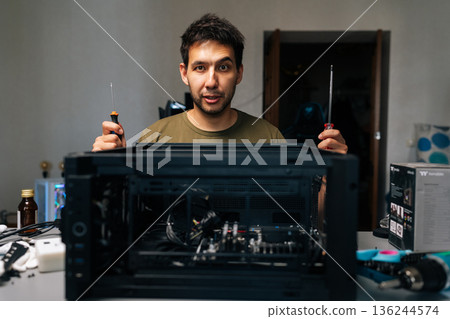 Computer professional working with screwdrivers during desktop computer assembly, demonstrating technical expertise in workplace environment with attention to detail, looking at camera. Computer professional working with screwdrivers during desktop computer assembly, demonstrating technical expertise in workplace environment with attention to detail, looking at camera. 136244574