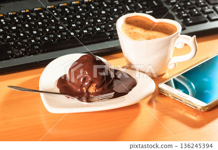 Cup of coffee and chocolate cake next to computer. 136245394