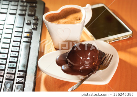 Cup of coffee and chocolate cake next to computer. 136245395