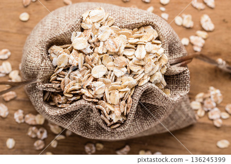 oat flakes cereal in burlap sack on wooden table. oat flakes cereal in burlap sack on wooden table. 136245399
