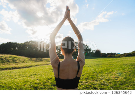 Practicing mindful yoga in a serene green field under the bright sun 136245643