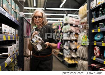 Older woman shopping for kitchen supplies in a well-organized store aisle during the daytime Older woman shopping for kitchen supplies in a well-organized store aisle during the daytime 136245804