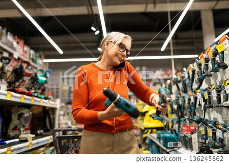 Woman shopping for power tools while talking on the phone in a hardware store during the day 136245862