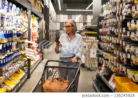 Woman shopping for supplies in a hardware store while using her smartphone 136245926