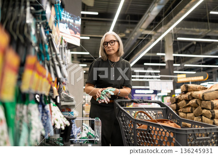 Middle-aged woman shopping at a modern grocery store during the day with a cart full of groceries 136245931