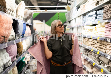Woman shopping for home textiles at a store, selecting cozy fabrics among colorful shelves Woman shopping for home textiles at a store, selecting cozy fabrics among colorful shelves 136245947