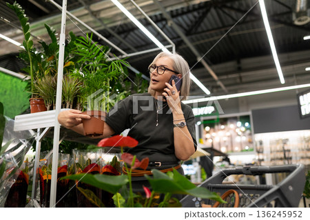 Woman shopping for plants while talking on her phone in a bright indoor garden center Woman shopping for plants while talking on her phone in a bright indoor garden center 136245952