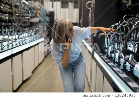 Woman examines kitchen faucets while on phone in a home improvement store during daylight 136245953