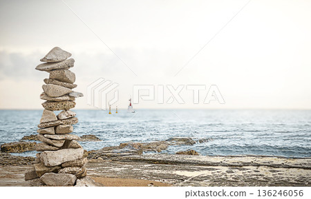 A stone pyramid of flat stones on a rocky seashore. 136246056