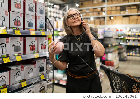 Woman shopping for kitchen appliances while talking on a smartphone at a retail store Woman shopping for kitchen appliances while talking on a smartphone at a retail store 136246061