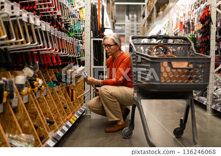 Older woman shopping for tools in a well-organized home improvement store aisle during the day Older woman shopping for tools in a well-organized home improvement store aisle during the day 136246068