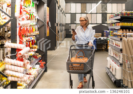 Senior woman shopping in a home improvement store while checking her phone 136246101