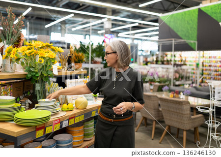 Woman shopping for tableware and home decor in a vibrant store filled with flowers and plants in 136246130