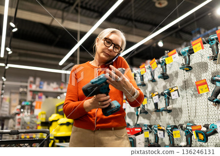 Woman shopping for tools in a hardware store while talking on the phone during a busy afternoon Woman shopping for tools in a hardware store while talking on the phone during a busy afternoon 136246131